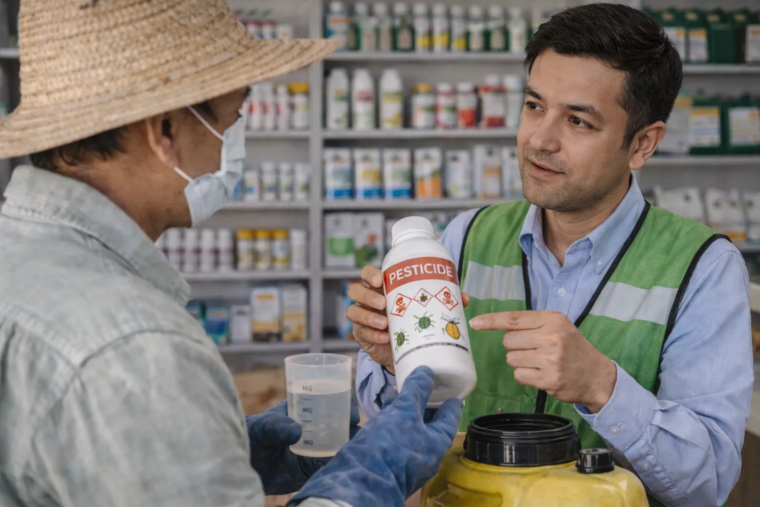 کشاورز در حال مشاوره با یک متخصص کشاورزی درباره سمها در یک فروشگاه عرضه محصولات کشاورزی، در حال بررسی سم شیمیایی با دقت www.nahalvand.com
